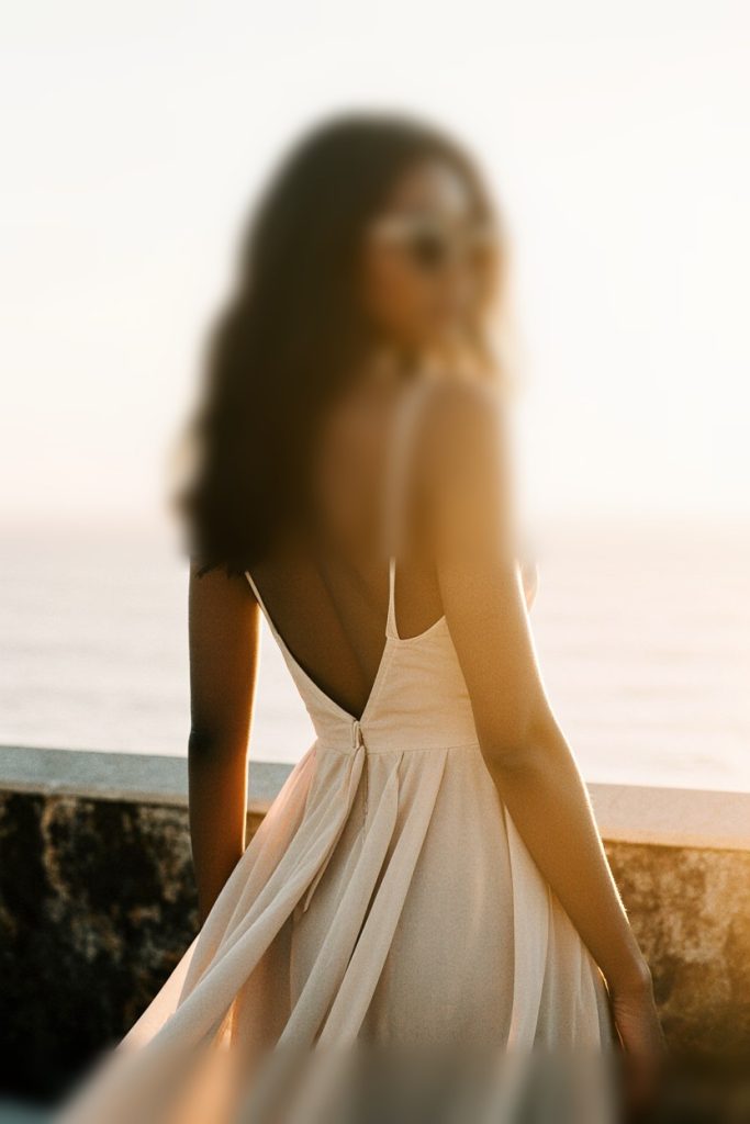 Elegant woman in white backless dress facing the ocean.